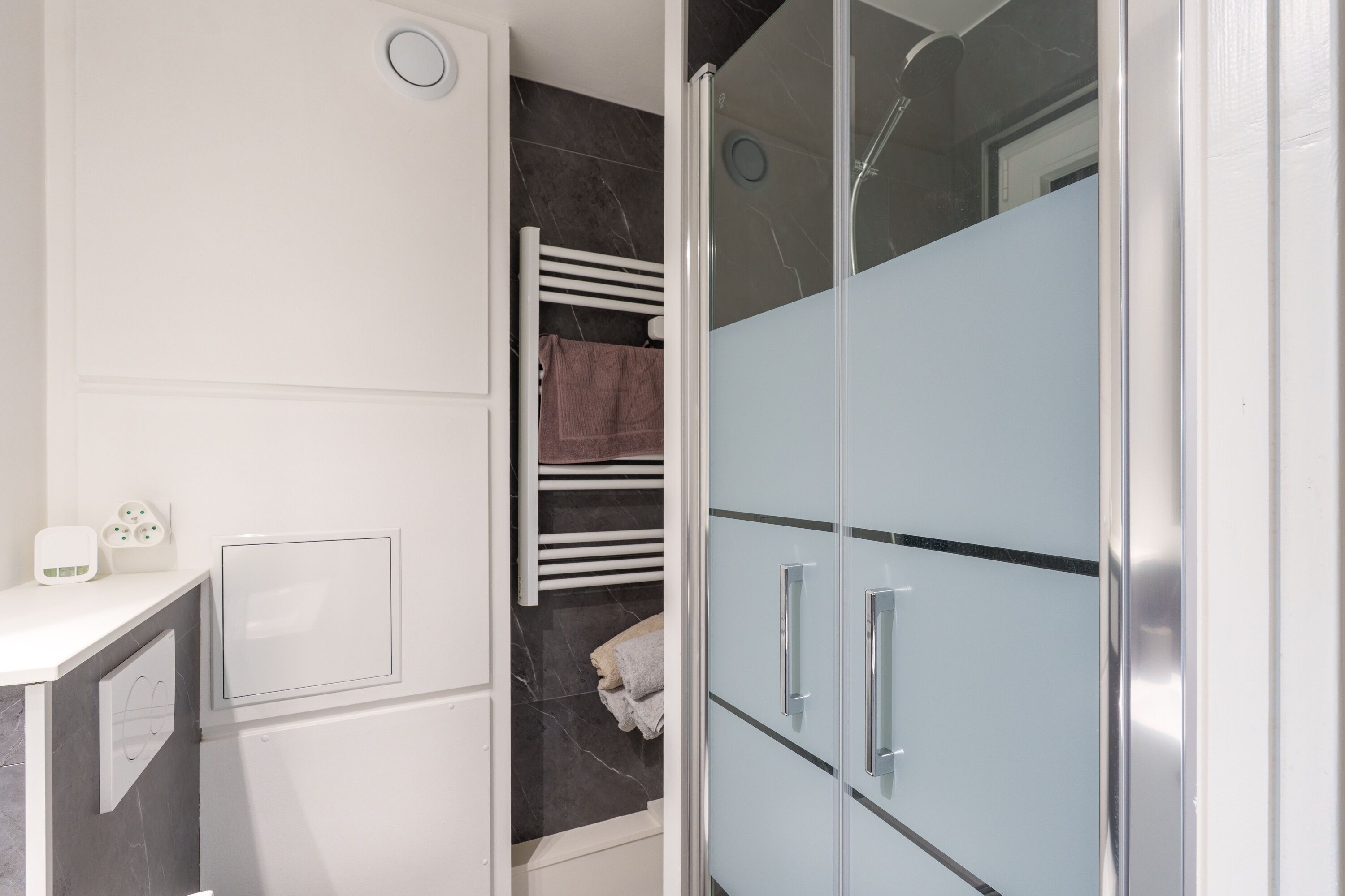 A modern bathroom with a white vanity, a glass shower enclosure, and a marble-tiled wall.
