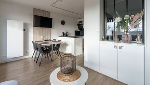 A modern kitchen with a dining area, a large window with decorative plants, and a white cabinet with a vase. - La Résidence Le Belvédère - Avec Balcon (Le Tholy)