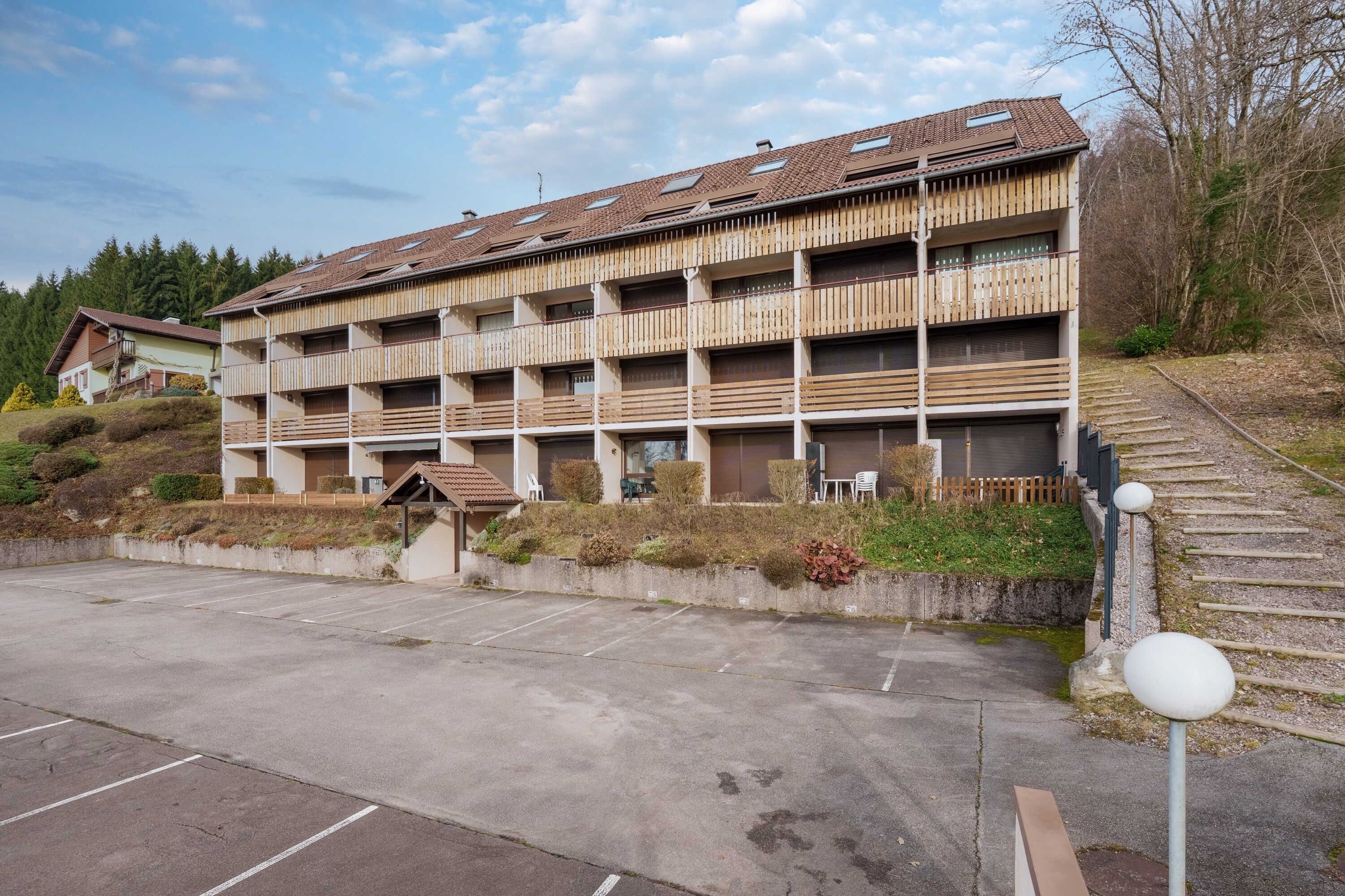 A multi-story building with a wooden facade, a parking lot, and a staircase leading up to the building.