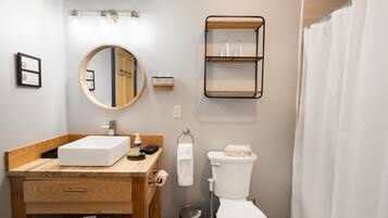 A bathroom with a wooden vanity, a round mirror, a toilet, and a shower curtain.