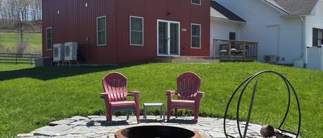 A red house with a fire pit and two Adirondack chairs in the front yard.