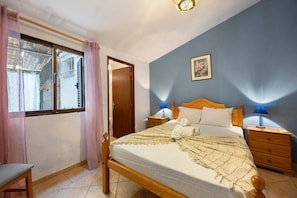 A bedroom with a bed, bedside tables, a chair, a window with curtains, and a door. - Holiday Home 'Buganvília' with Shared Pool and Wi-Fi (Luz)