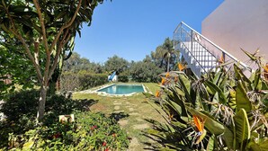Una piscina rodeada de exuberante vegetación, una escalera que conduce a un edificio y diversas plantas tropicales.