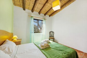 Une chambre à coucher avec un lit, une table de chevet avec une lampe, une chaise et une fenêtre avec des rideaux.