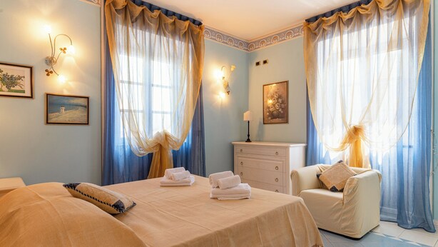 Ein Hotelzimmer mit einem Bett, einem Sessel, einem Schminktisch und zwei fensterbepflanzten Fenstern.