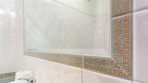 Ein Badezimmer mit Waschbecken in Weiß, goldenem Wasserhahn und dekorativen Fliesen mit geometrischem Muster.
