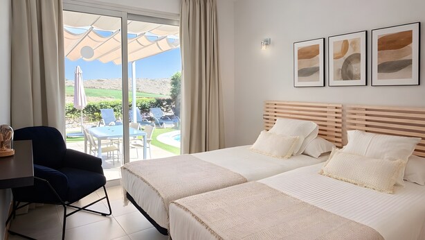 Une chambre d’hôtel avec deux lits, un bureau et une vue sur une piscine et un espace de détente extérieur.
