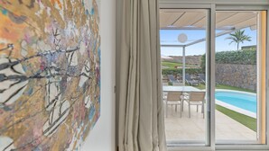 Une pièce agrémentée d’un grand tableau abstrait, avec une porte-fenêtre coulissante donnant sur un espace extérieur comprenant une piscine et du mobilier de jardin.