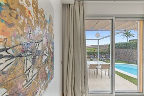 Una stanza con un quadro astratto di grandi dimensioni, una porta scorrevole in vetro che dà su un'area esterna con piscina e mobili da patio.