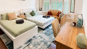 Une chambre avec deux lits, un bureau en bois, une chaise, une grande fenêtre avec des volets et un luminaire décoratif au plafond.