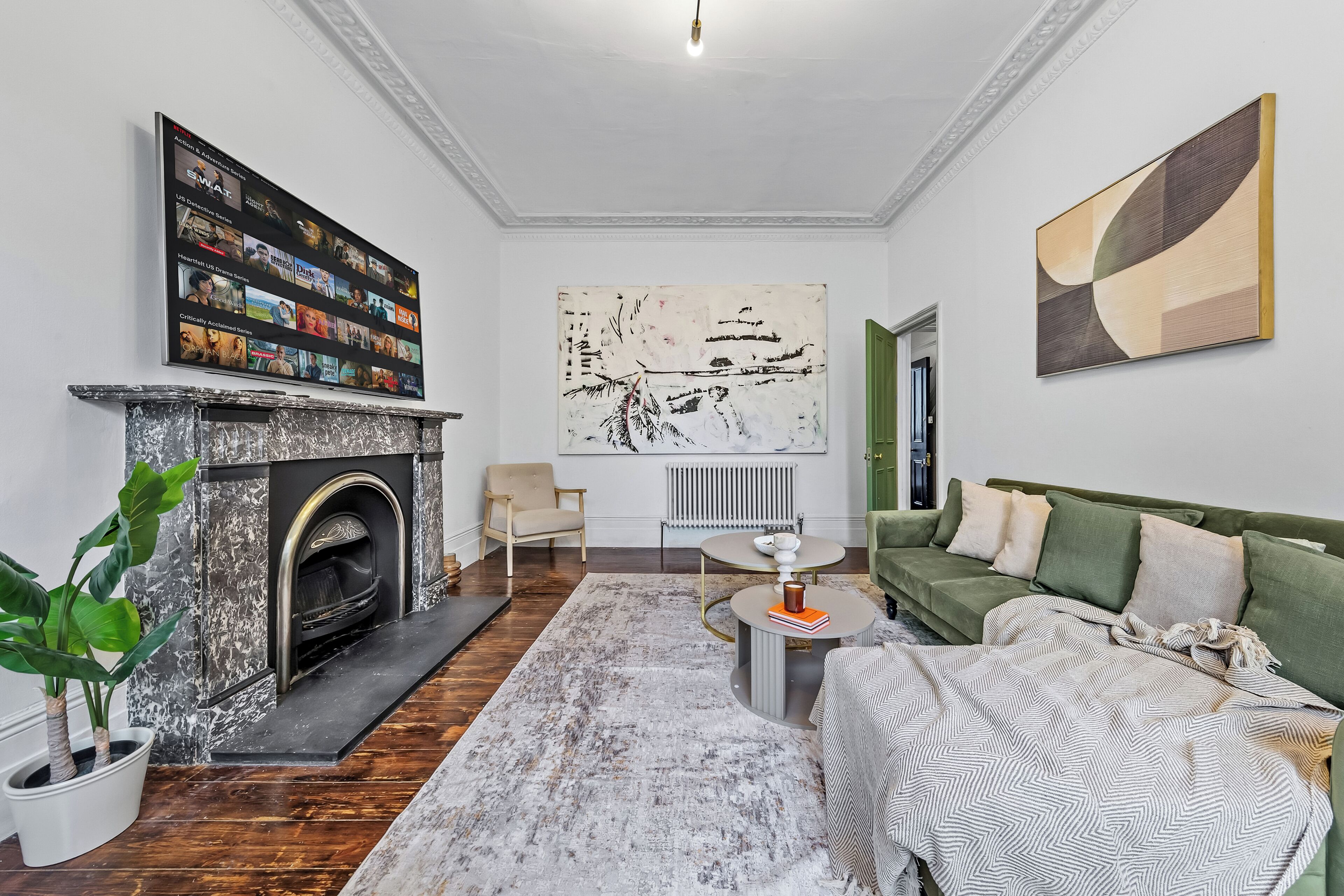 Una sala de estar moderna con chimenea, un sofá verde, una mesa de centro y un cuadro abstracto grande en la pared.