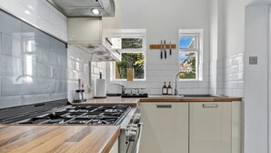Une cuisine moderne équipée d’une cuisinière à gaz, d’un plan de travail en bois, de meubles blancs et d’une fenêtre donnant sur l’extérieur.