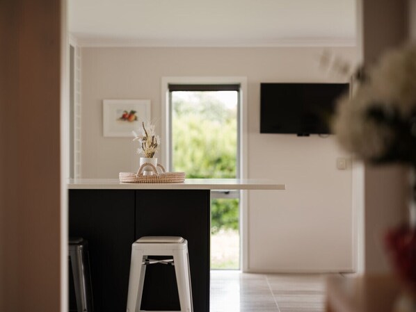 Una cocina moderna con encimera blanca, un taburete pequeño y una cesta con plantas secas.
