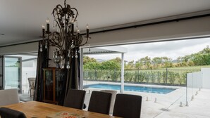 A dining area with a view of a swimming pool and a garden. - ⭐️ The Wine Country Retreat by Homello ⭐️ | Pool • Wineries • Wedding Venues (Kumeū)