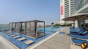 Ein Poolbereich auf dem Dach mit Liegestühlen, einem Pool mit blauen Mosaikfliesen und Blick auf die Stadt.