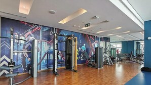 Ein Fitnessraum mit unterschiedlichen Trainingsgeräten, Holzboden und blauer Wand mit Wandgemälde.
