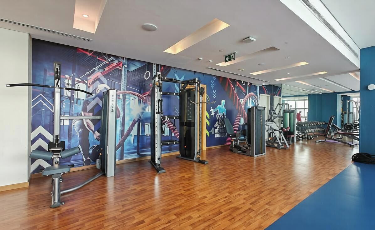 Een sportschool met diverse fitnessapparaten, een houten vloer en een blauwe muur met een muurschildering.