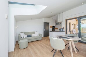 Un appartement moderne doté d’un plafond de style industriel, d’un coin repas avec une table ronde et des chaises, d’un canapé et d’un espace cuisine.