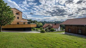 Un edificio moderno con tetto spiovente e facciata in legno, circondato da un'area verde e altri edifici residenziali.