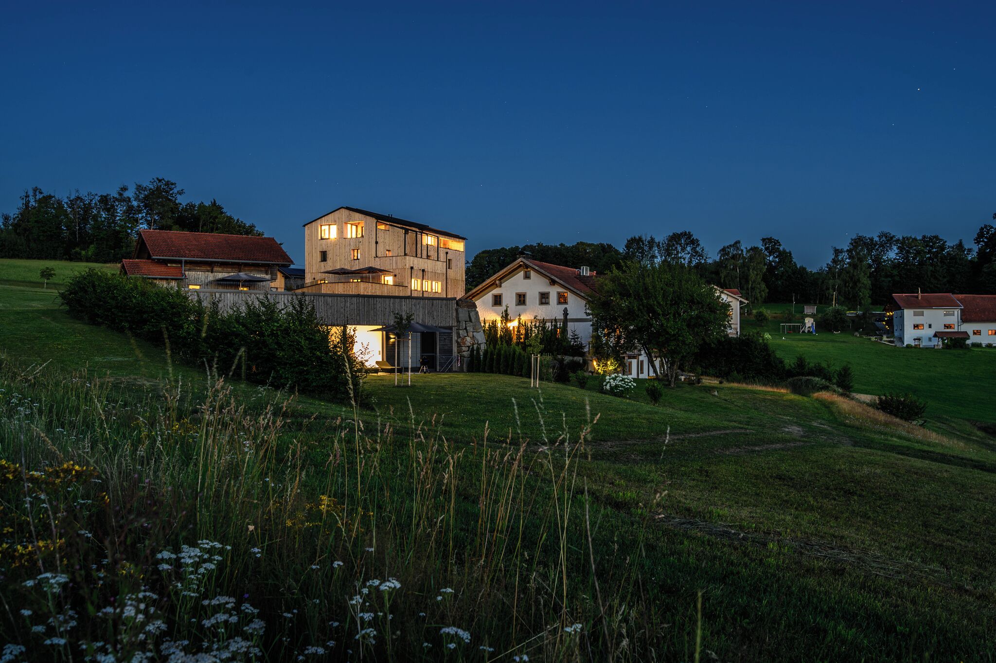 Paisatge rural amb una casa gran de dos pisos i edificis més petits, envoltat de camps i arbres.