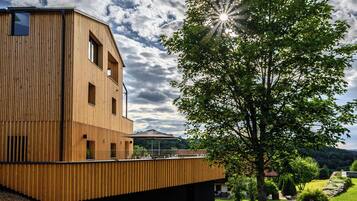 Ein modernes Holzgebäude mit geneigtem Dach, einem gepflasterten Weg und einem Baum im Vordergrund.