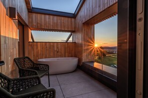 Un espacio exterior moderno con terraza de madera, jacuzzi y zona de estar con sillas.