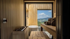 Een sauna met een houten bank, een bank met handdoeken, en uitzicht op het landschap.