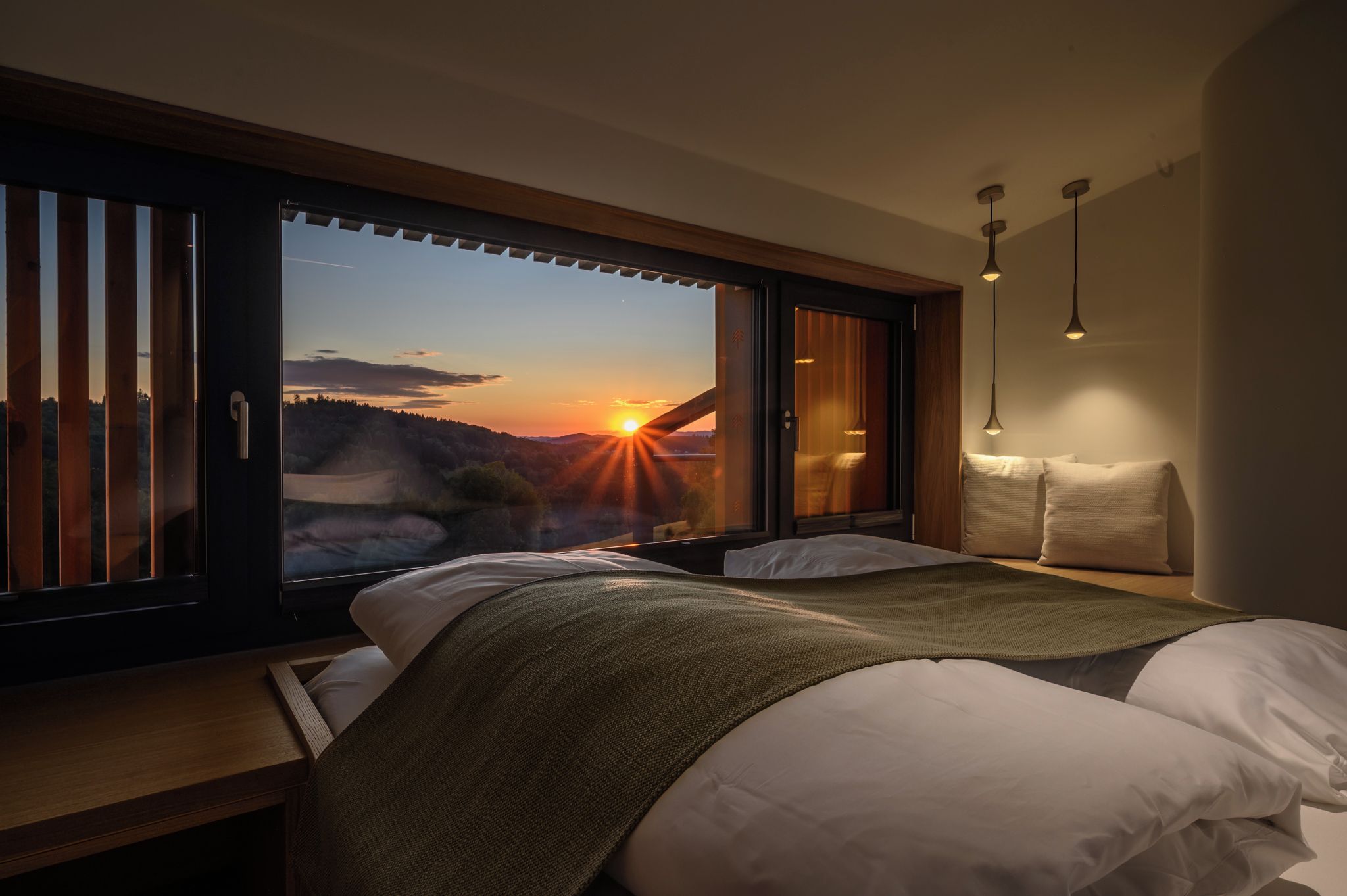Un dormitorio con una ventana grande, una cama, mesitas de noche y una lámpara colgante.