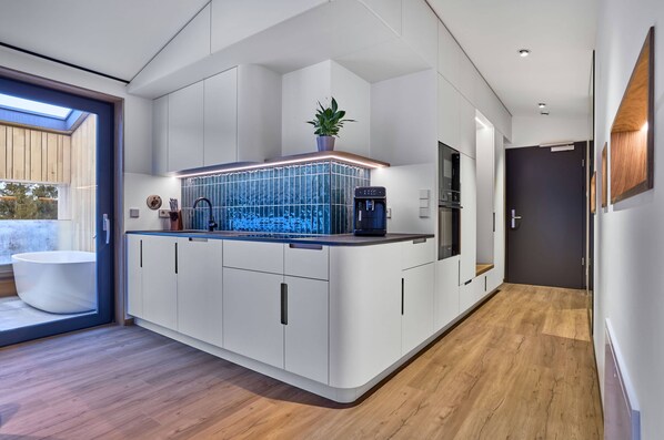 A modern kitchen with white cabinetry, a built-in island with a blue backsplash, and a skylight.