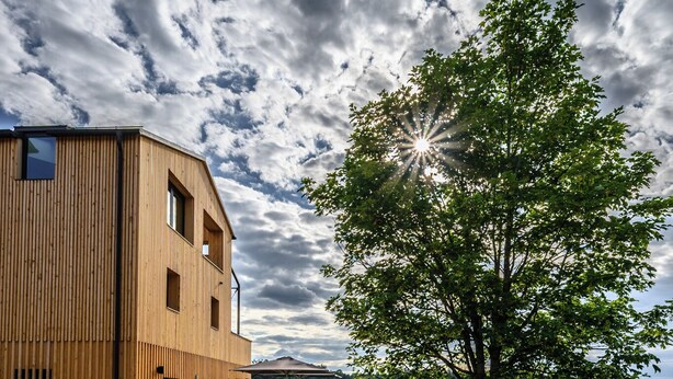 A modern wooden building with a sloped roof, a paved pathway, and a tree in the foreground. - Modern design apartment with a view of the valley.<br>With sauna, roof terrace, outdoor bathtub and custom-made furnishings.<br>Perfect for two adults who appreciate peace and quality. (Breitenberg)