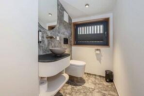 A modern bathroom with a marble sink, a toilet, and a window with blinds.