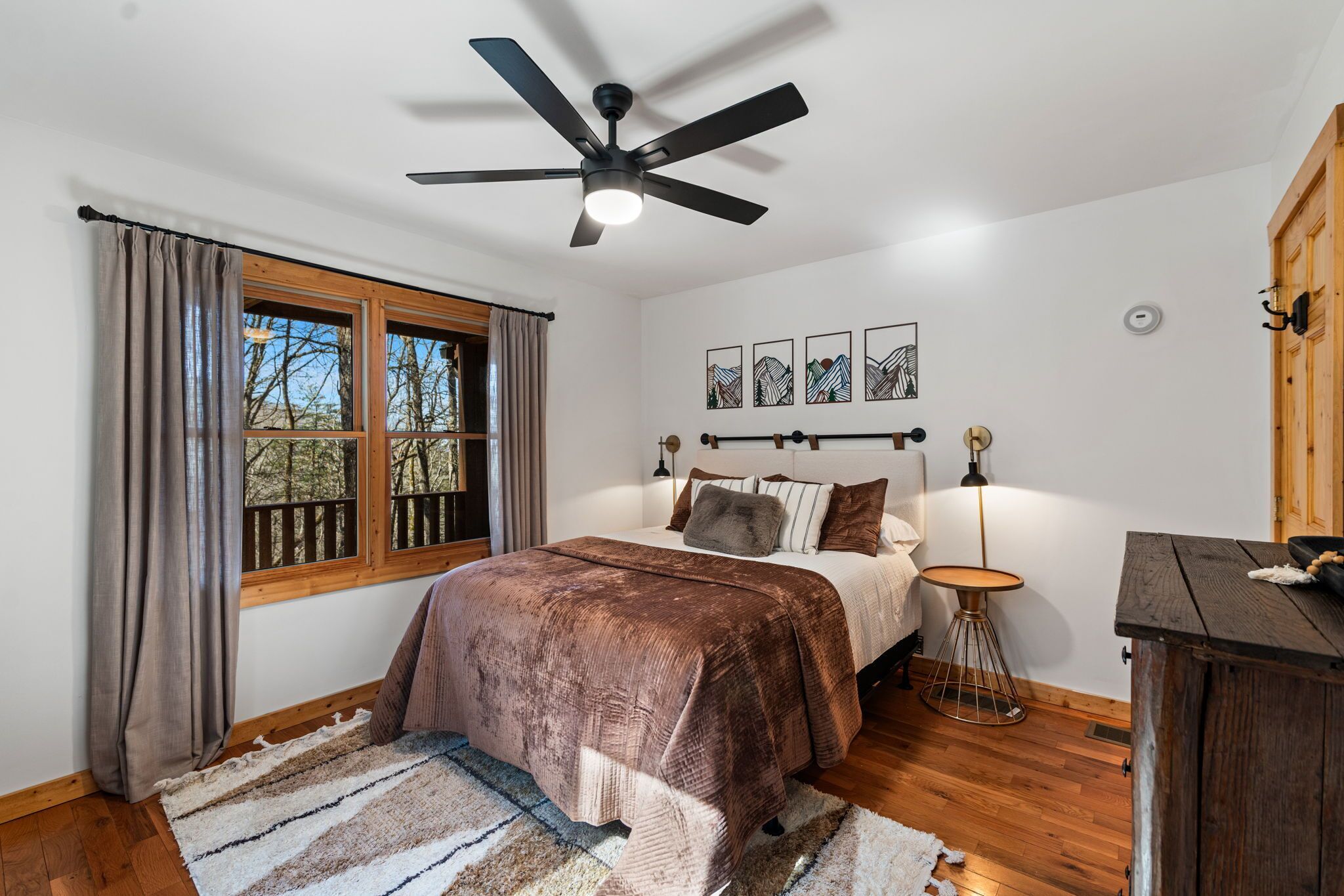 Un dormitorio con cama, ventilador de techo, ventana con cortinas, mesita de noche y decoración en la pared.
