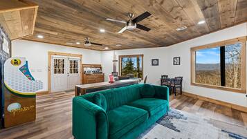 A spacious living area with a green sofa, wooden ceiling, and a view of the outdoors through a large window.