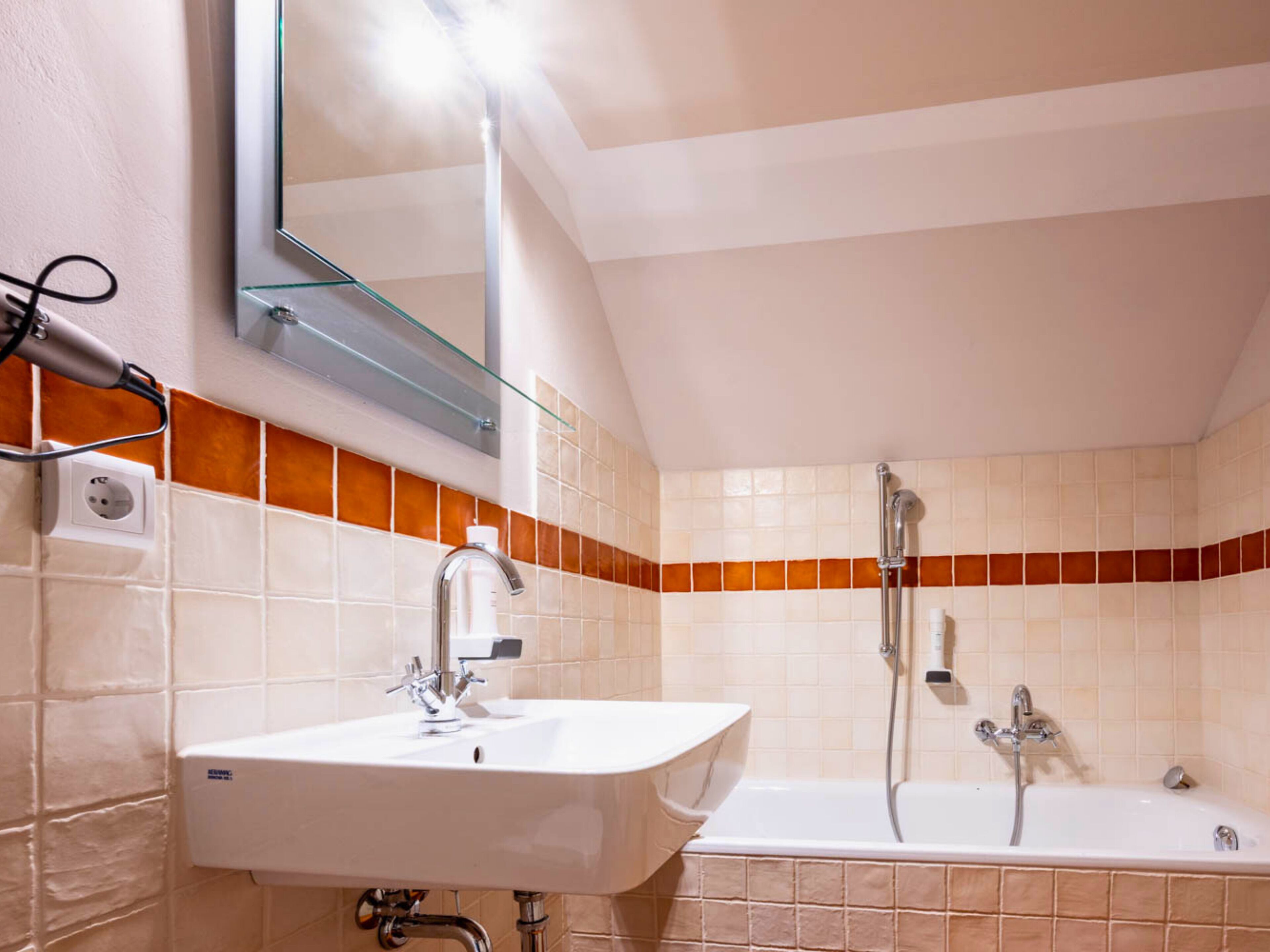 Ein Badezimmer mit weißem Waschbecken, einem Spiegel, einer Dusche und orangefarbenen Fliesen.