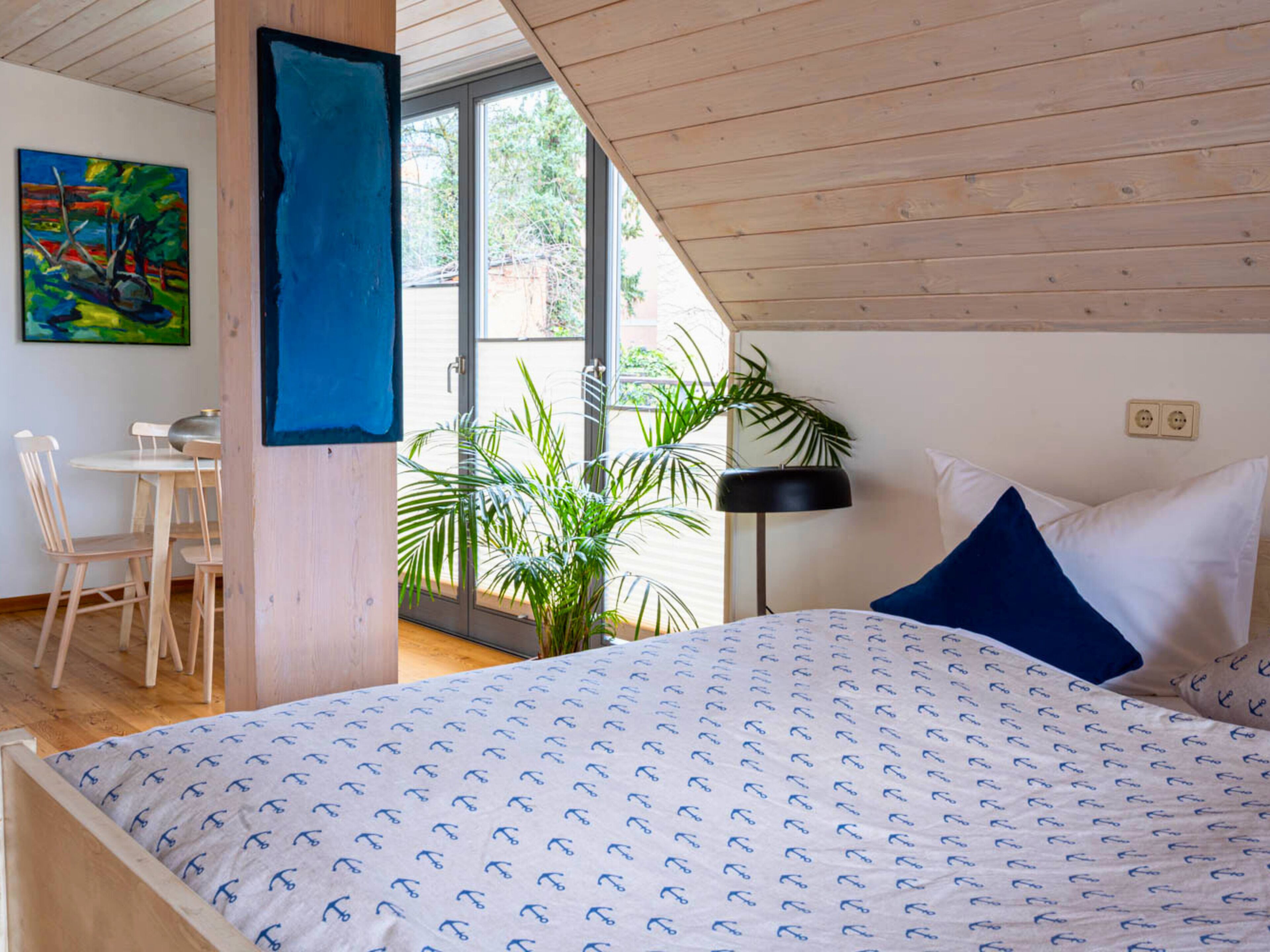 A bedroom with a bed, a desk, and a chair. There is a window with a view of greenery outside.