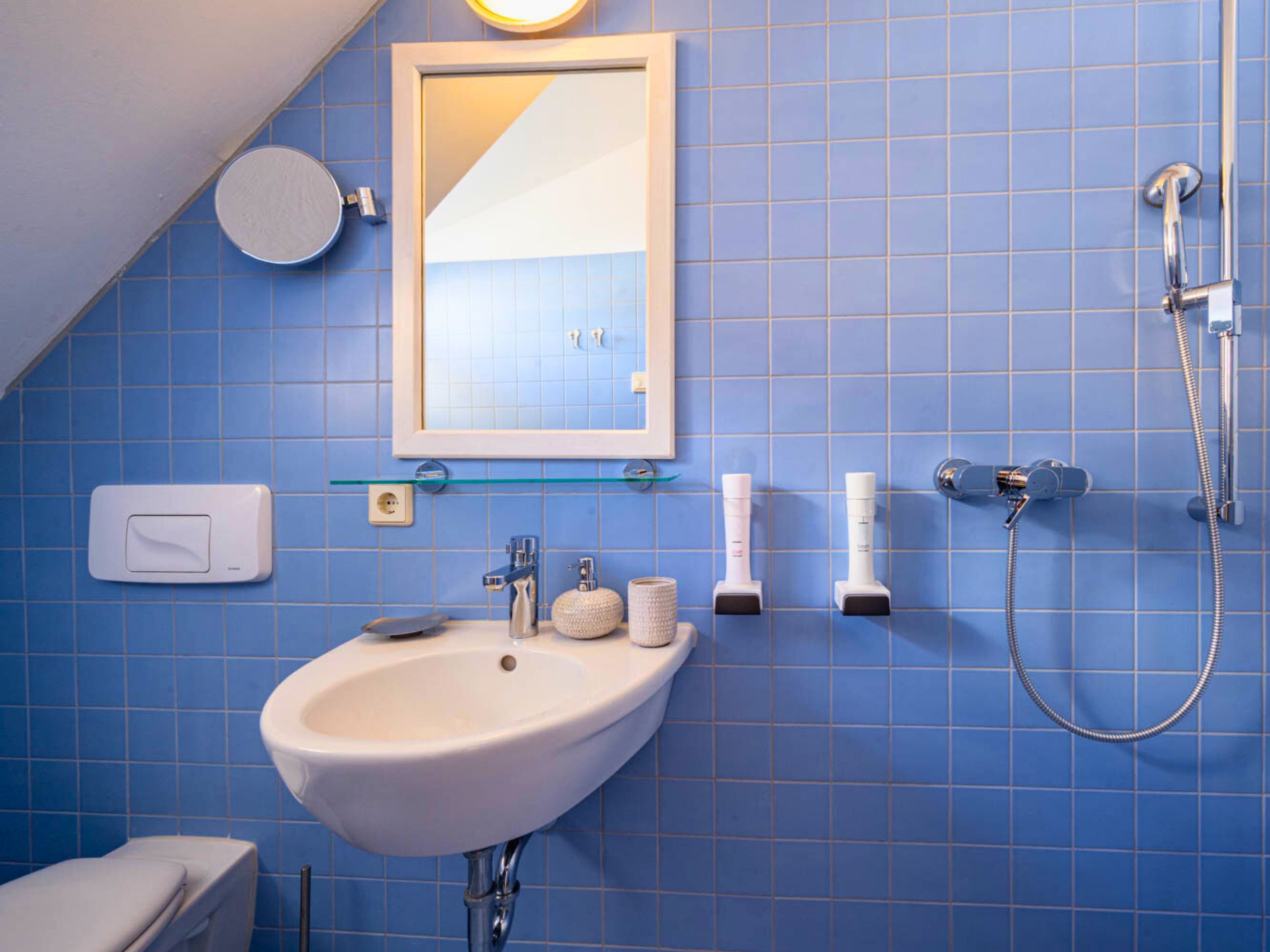 A bathroom with a white sink, a mirror, a shower, and a toilet.