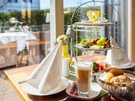 A three-tiered dessert stand with fruits and a glass of beverage on a table.