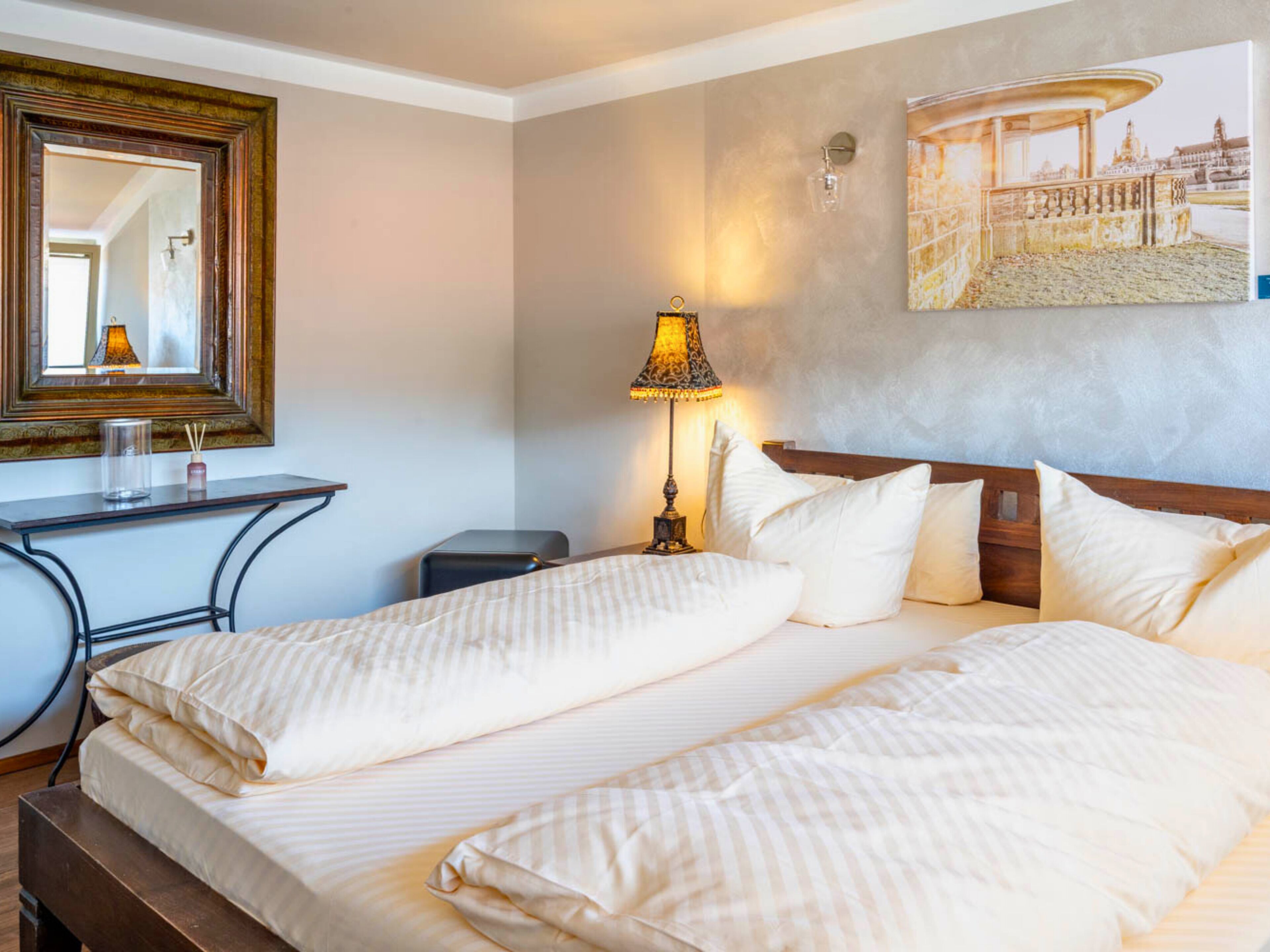 A hotel room with a large bed, a desk, a chair, a lamp, and a painting on the wall.