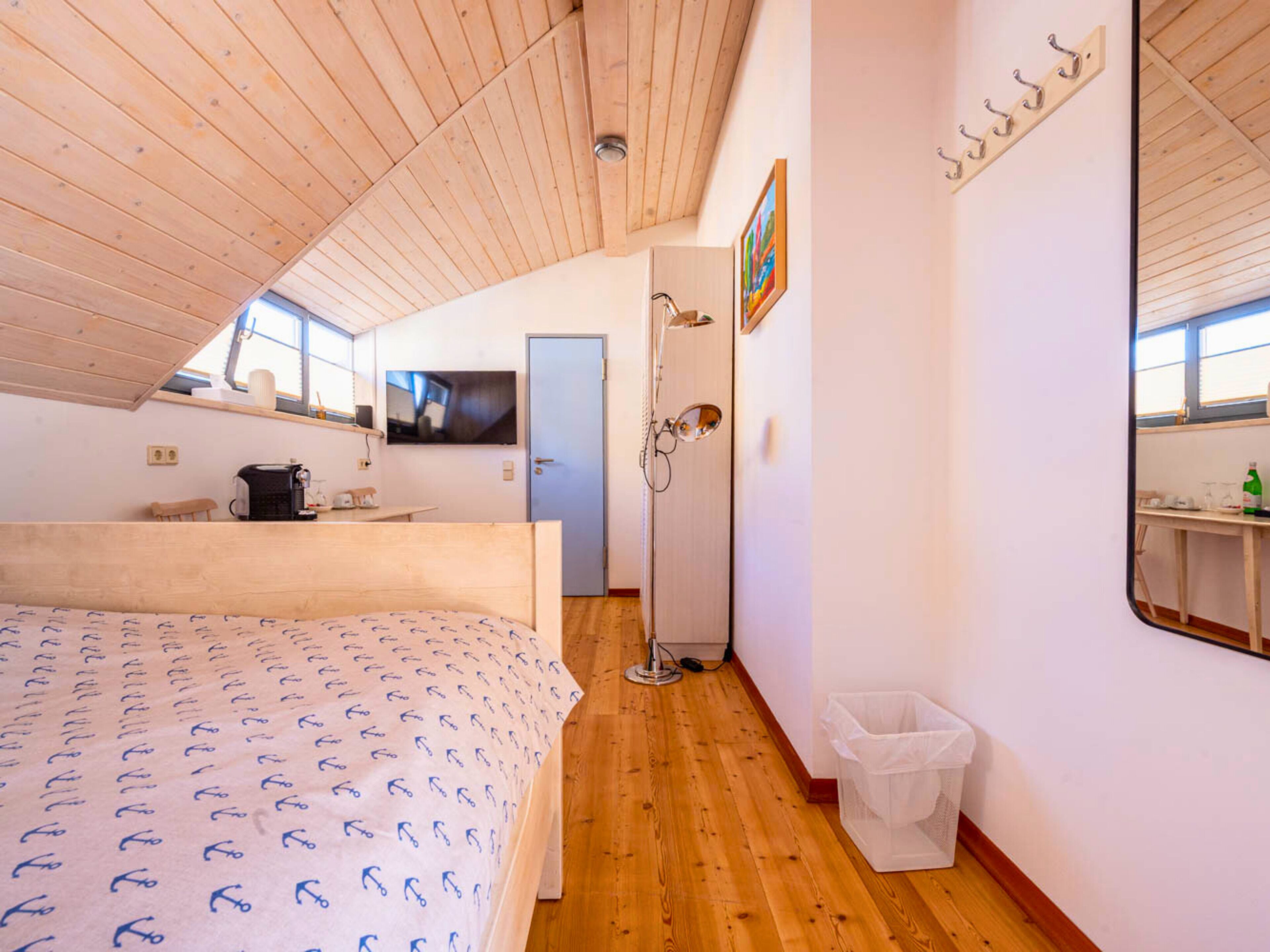 Ein Schlafzimmer mit Holzboden, einem Bett mit gemustertem Überwurf, einem Fernseher, einem kleinen Tisch mit Wasserkocher und einer Tür zu einem Badezimmer.