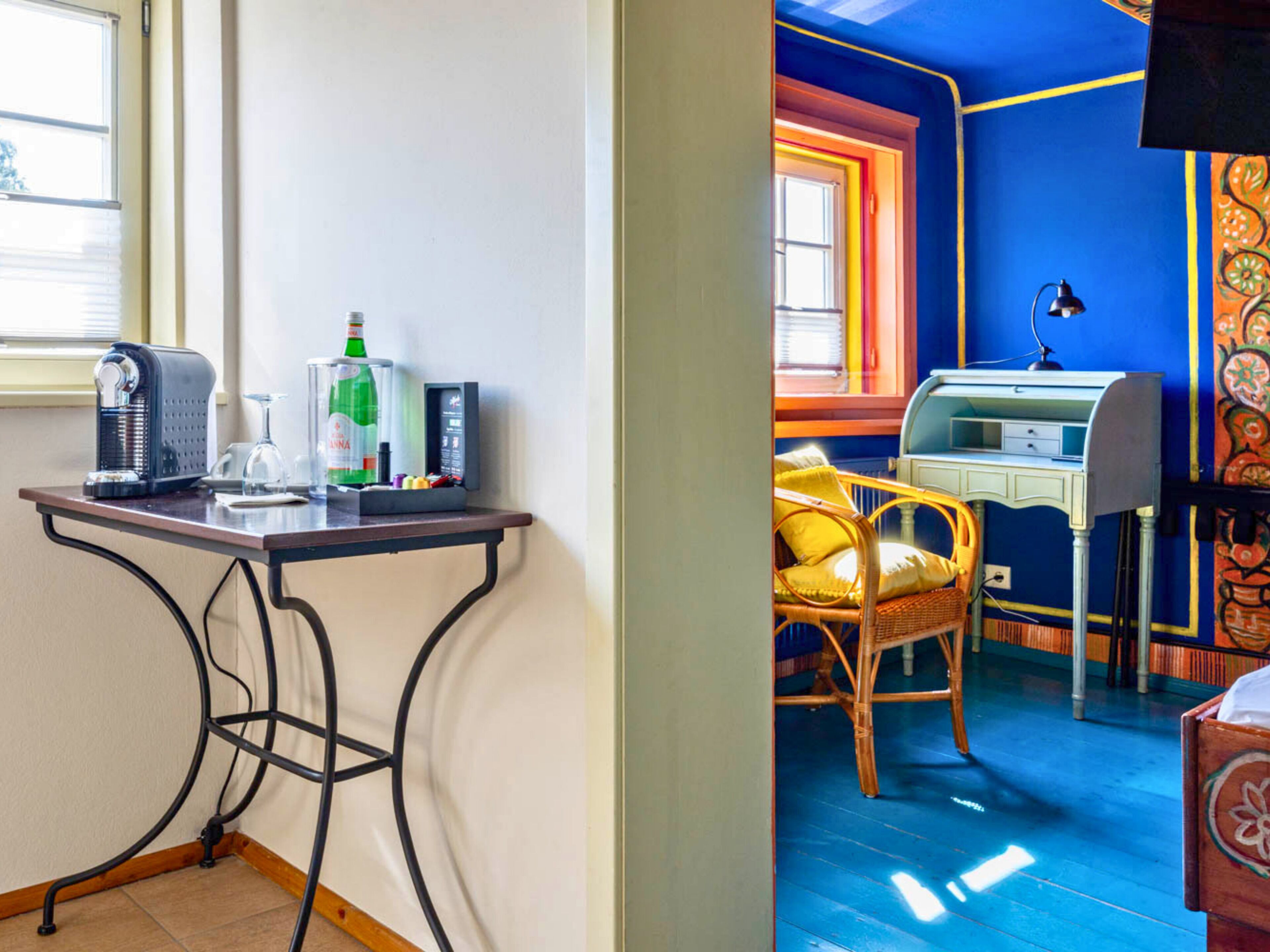 A room with a desk, chair, and a small table with a bottle and a glass.