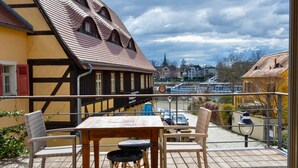 A balcony with a table and chairs, overlooking a street with parked cars and buildings. - La Campagnola - Ristorante&Boutiquehotel (Dresden)