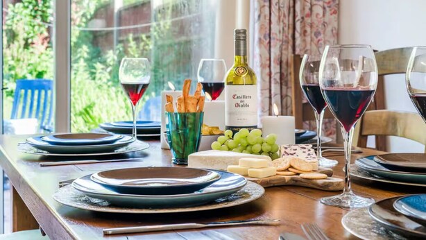 A dining table set with plates, glasses, a bottle of wine, cheese, crackers, and grapes. - Perfect 4-bedroom house in Oadby for a relaxing stay (Oadby)