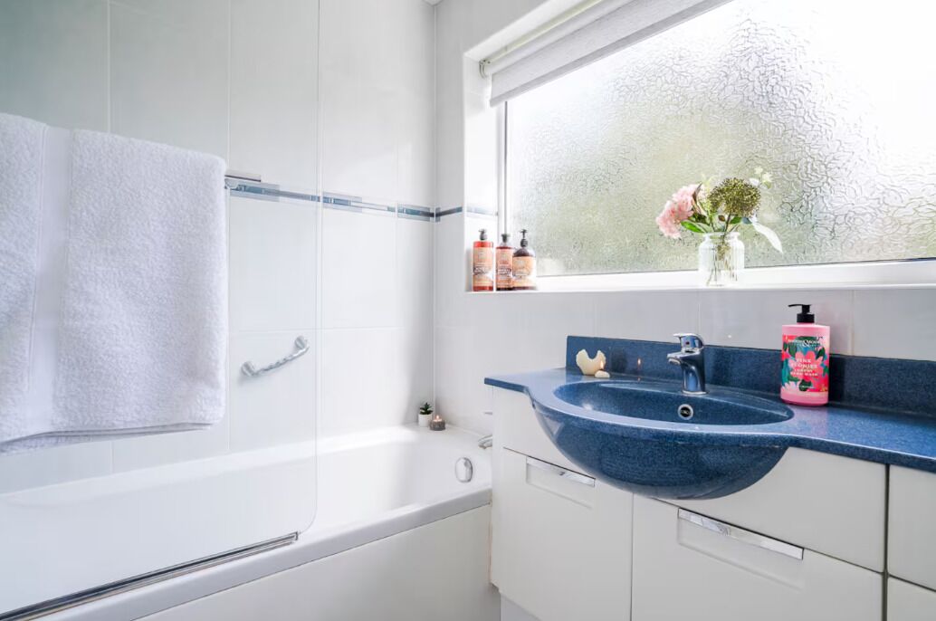 A modern bathroom with a bathtub, a blue sink, and a window with a frosted glass view.