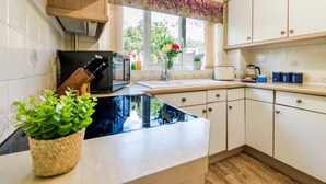 A modern kitchen with white cabinets, a black countertop, and a window with a floral curtain. - Perfect 4-bedroom house in Oadby for a relaxing stay (Oadby)