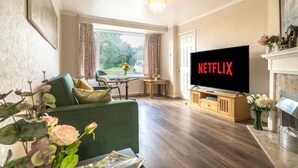 A living room with a television displaying "NETFLIX," a green sofa, a wooden coffee table, and a fireplace. - Perfect 4-bedroom house in Oadby for a relaxing stay (Oadby)
