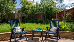 Two blue chairs with cushions, a small table with a bowl and glasses, and a wooden fence in a garden setting. - Perfect 4-bedroom house in Oadby for a relaxing stay (Oadby)