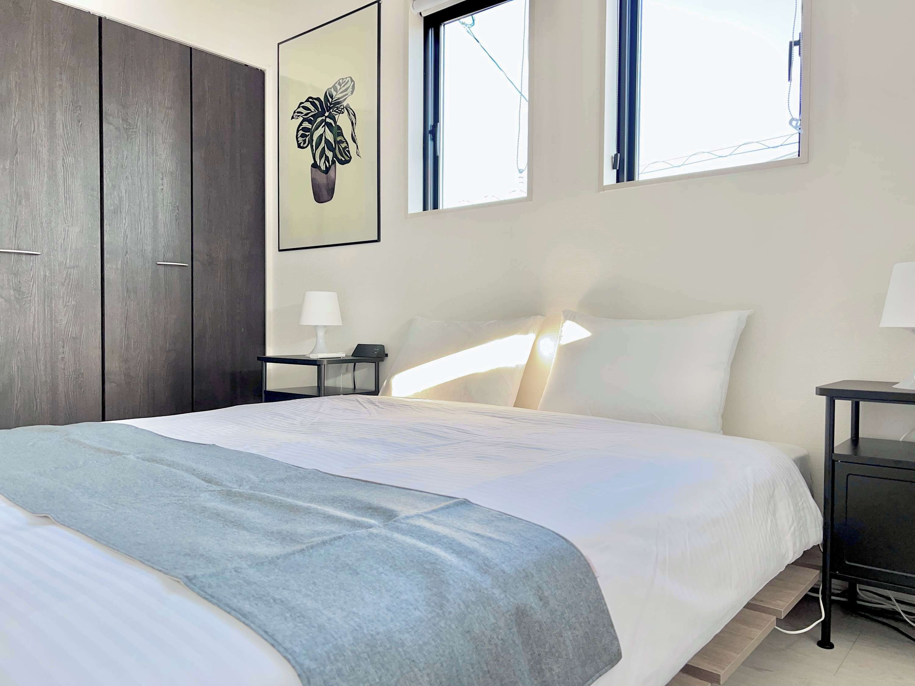 A hotel room with a bed, bedside tables, a nightstand, a window, and a wall-mounted artwork.