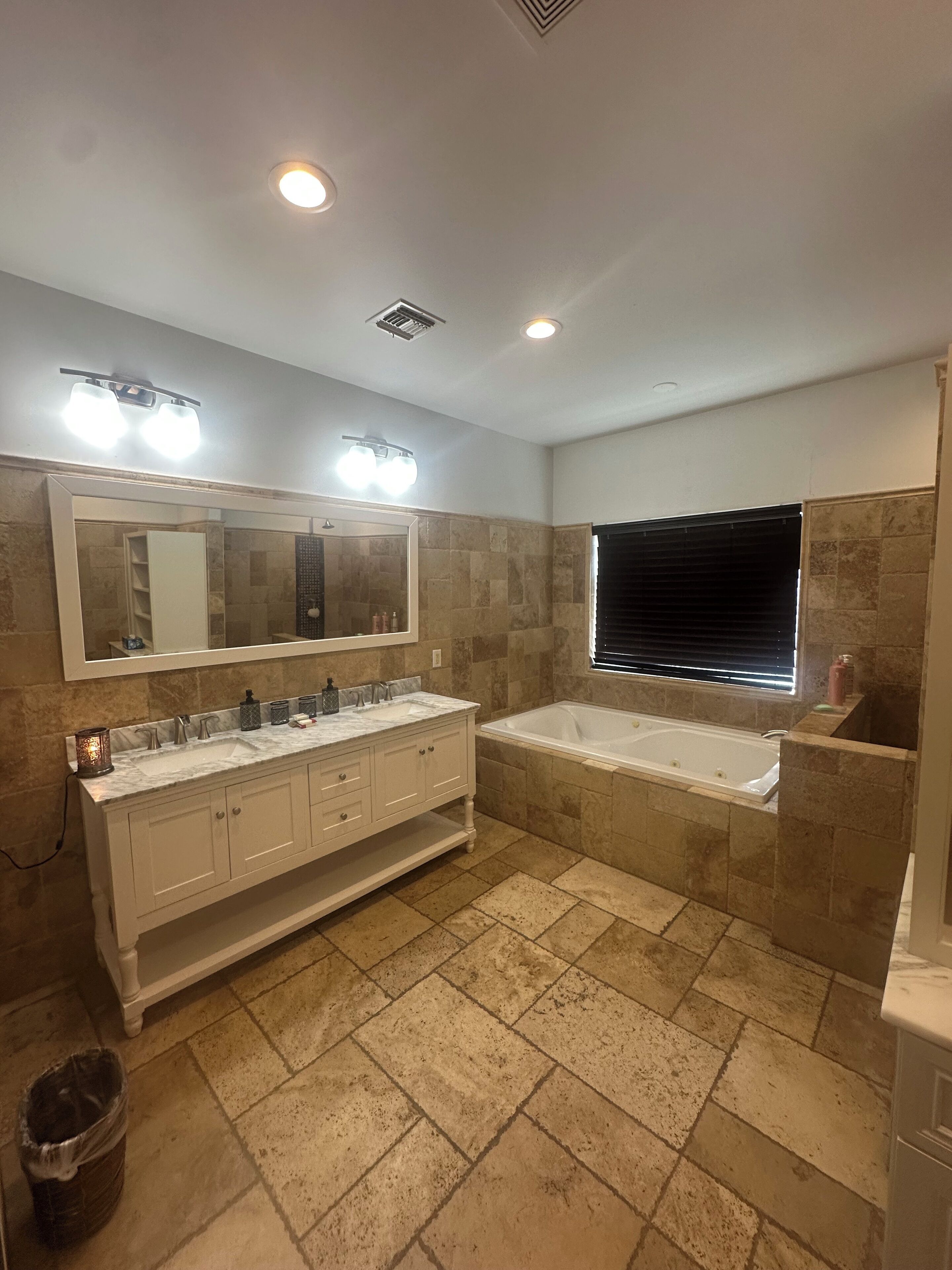 Un baño con lavamanos doble, un espejo grande, una bañera y una ventana con persianas.