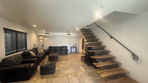 Un vaste espace de vie agrémenté d’un escalier moderne, de canapés en cuir et d’un sol carrelé.