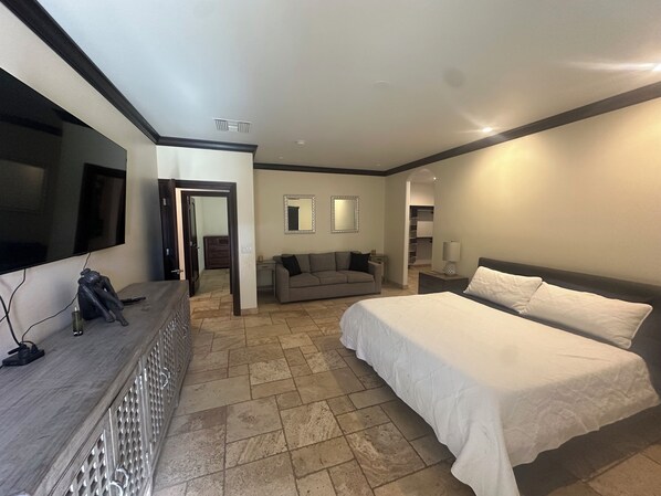 A hotel room with a large bed, a sofa, a TV, and a desk with a mirror.